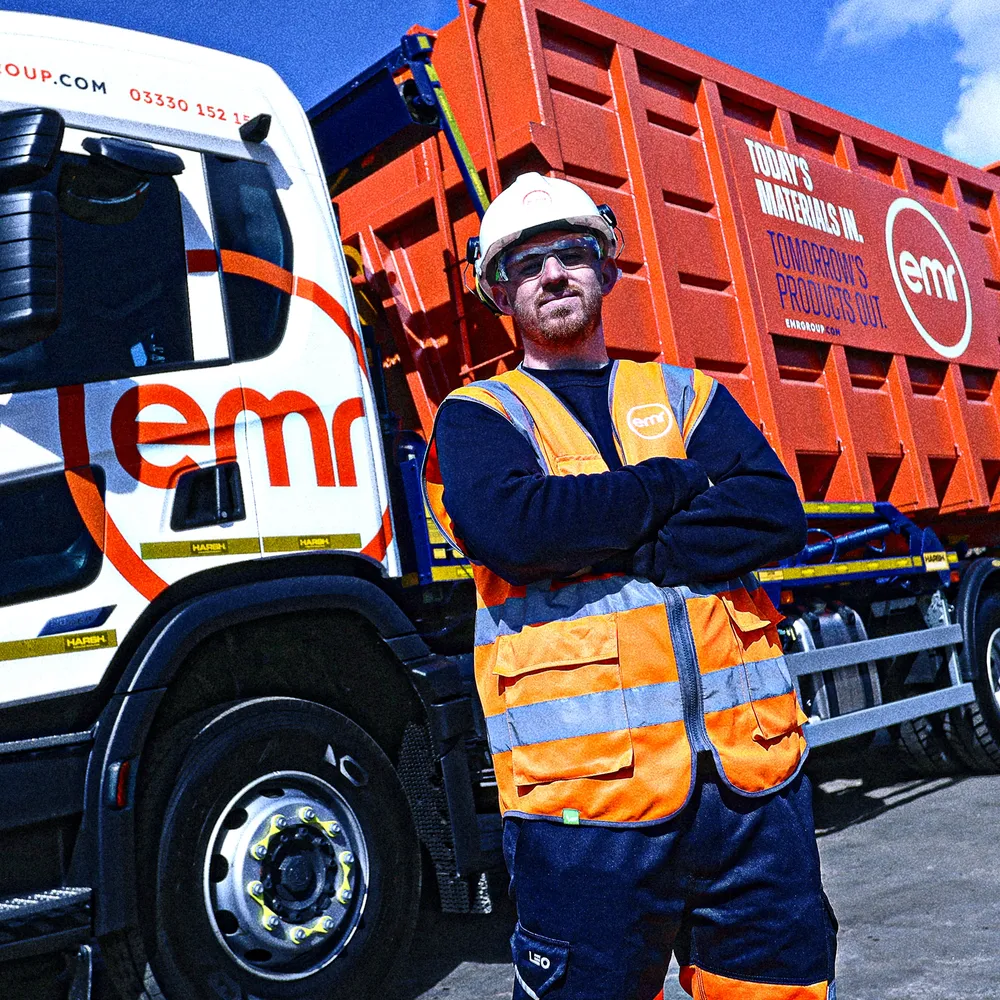 A person wearing a hard hat and safety vest stands in front of a red and white truck.
